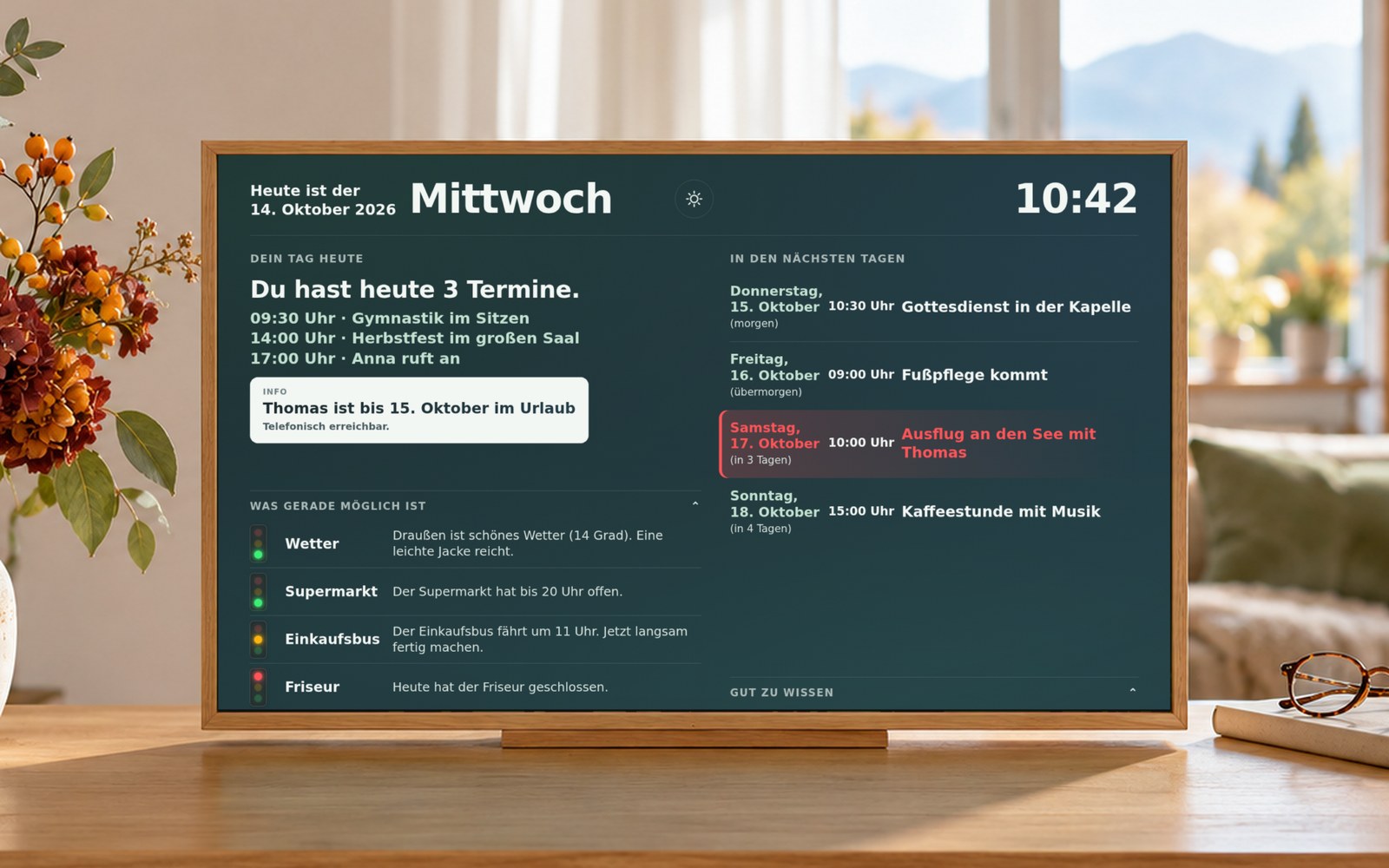 CareScreen auf einer hellen Holzkommode im Wohnzimmer. Der Schirm zeigt: Heute ist der 14. Oktober 2026, Mittwoch, 10:42 Uhr. Du hast heute 3 Termine: Gymnastik, Herbstfest, Anna ruft an. Darunter die Ampel: Wetter grün, Supermarkt grün, Einkaufsbus gelb, Friseur rot.